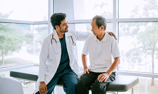 doctor speaking with a patient, the doctor's hand is on the patient's shoulder