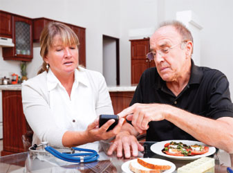 man and woman eating dinner, the woman is holding a glucose monitor for both of them to look at
