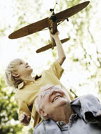 Child sitting on grandfather's shoulders while playing with a toy plane