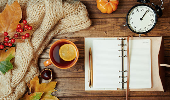 autumn table with calendar, alarm clock, tea and autumn decorations