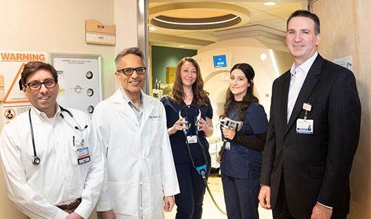 MRI technicians from left Lauren Goldman and Jessica Santa Maria hold the integrated audio-video headset used with MMC's new MRI-compatible audiovisual system. Also pictured from left, Chair of Pediatrics Dr. Jonathan Teitelbaum, Chair of Radiology Dr. Tejas Shinde, and Vice President of Clinical Operations Michael Perdoni.