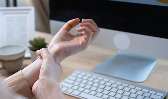person sitting in front of a computer and holding their wrist