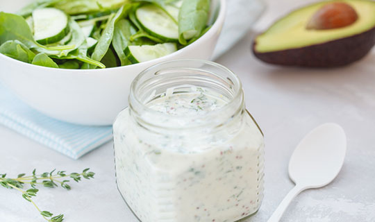 avocado ranch dressing in a jar with a salad and half of an avocado in the background