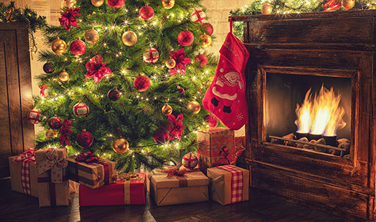 warmly lit Christmas tree with presents, next to a fireplace
