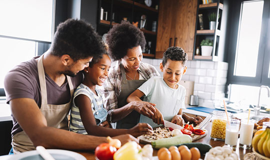 family working together in the kitchen to make a meal, mom and son are slicing tomatoes 