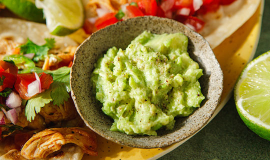 a bowl of guacamole surrounded by tacos