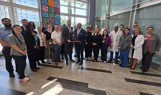 Jonathan P. Kyriacou, President and Chief Executive Officer of Jersey City Medical Center, accepts the 75-year membership award from the American Hospital Association’s Regional Executive, Michael Draine, joined by a diverse team of JCMC health professionals, including physicians, administrators, nurses, and ancillary staff