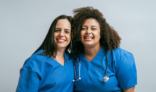 two nurses, in blue scrubs, smiling