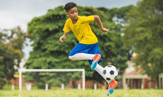 young boy jumping in the air while kicking a soccer ball