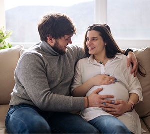 pregnant woman and her husband sitting on the couch smiling at each other
