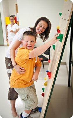 physical therapist helping young boy climb wall