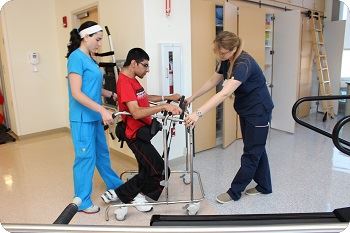 young man with walker being assisted to walk with medical professionals 