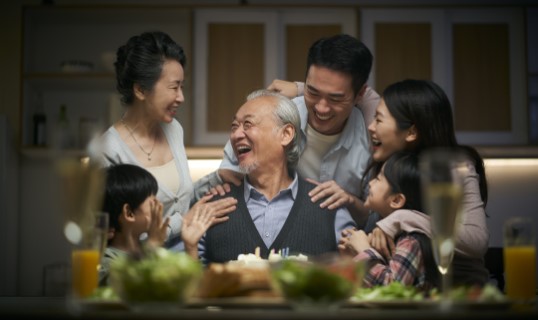 Multi-generational family celebrating their grandfather's birthday with a cake