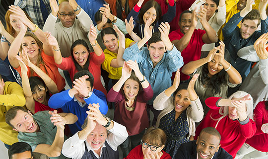 group of people with their hands raised above their heads clapping and smiling