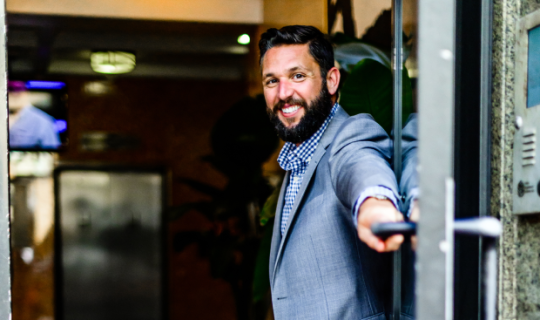 Smiling man holding the door for someone else