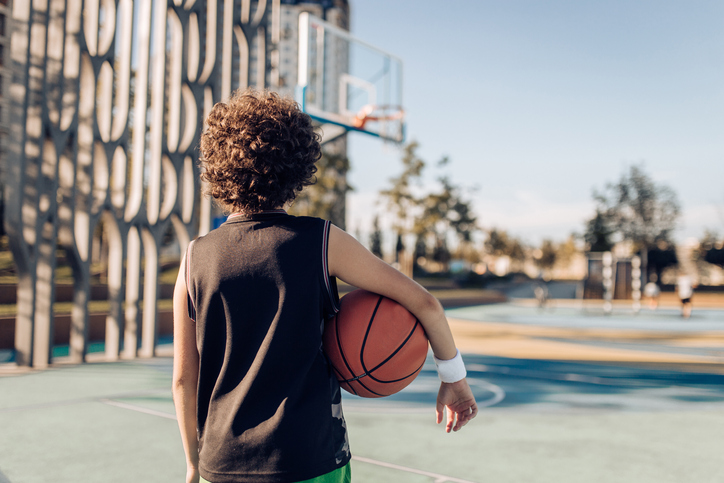 Boy facing away from the camera, showing his back, holding a basketball - scoliosis image
