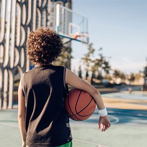 Boy facing away from the camera, showing his back, holding a basketball - scoliosis image