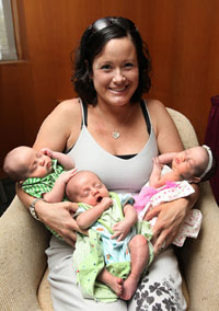 Smiling mother holding triplet newborn babies