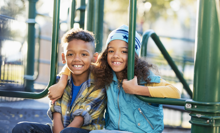 Multiracial siblings on playground smiling at camera